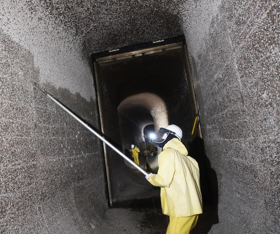 Photo of a person in safety gear scraping barnacle buildup along filling tunnels.