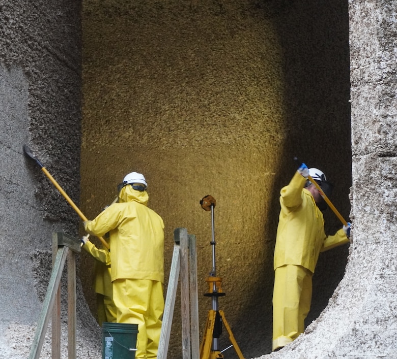 Photo of people in safety gear scraping barnacle buildup along filling tunnels.