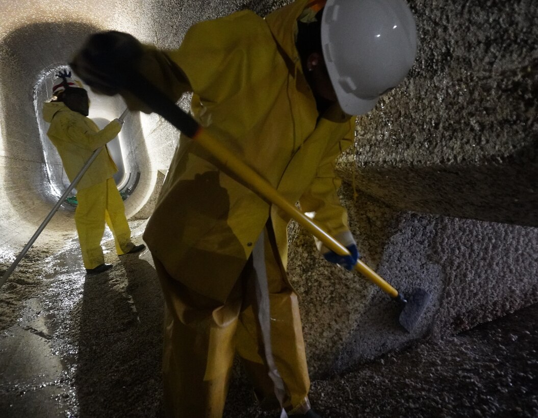 A Corps of Engineers employee scrapes barnacle buildup along the 14-foot-tall filling tunnels at Lake Washington Ship Canal and Hiram M. Chittenden Locks.