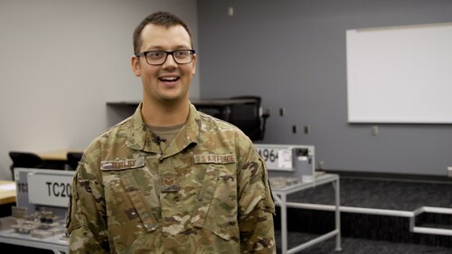 An Airman smiles at the camera in a classroom.