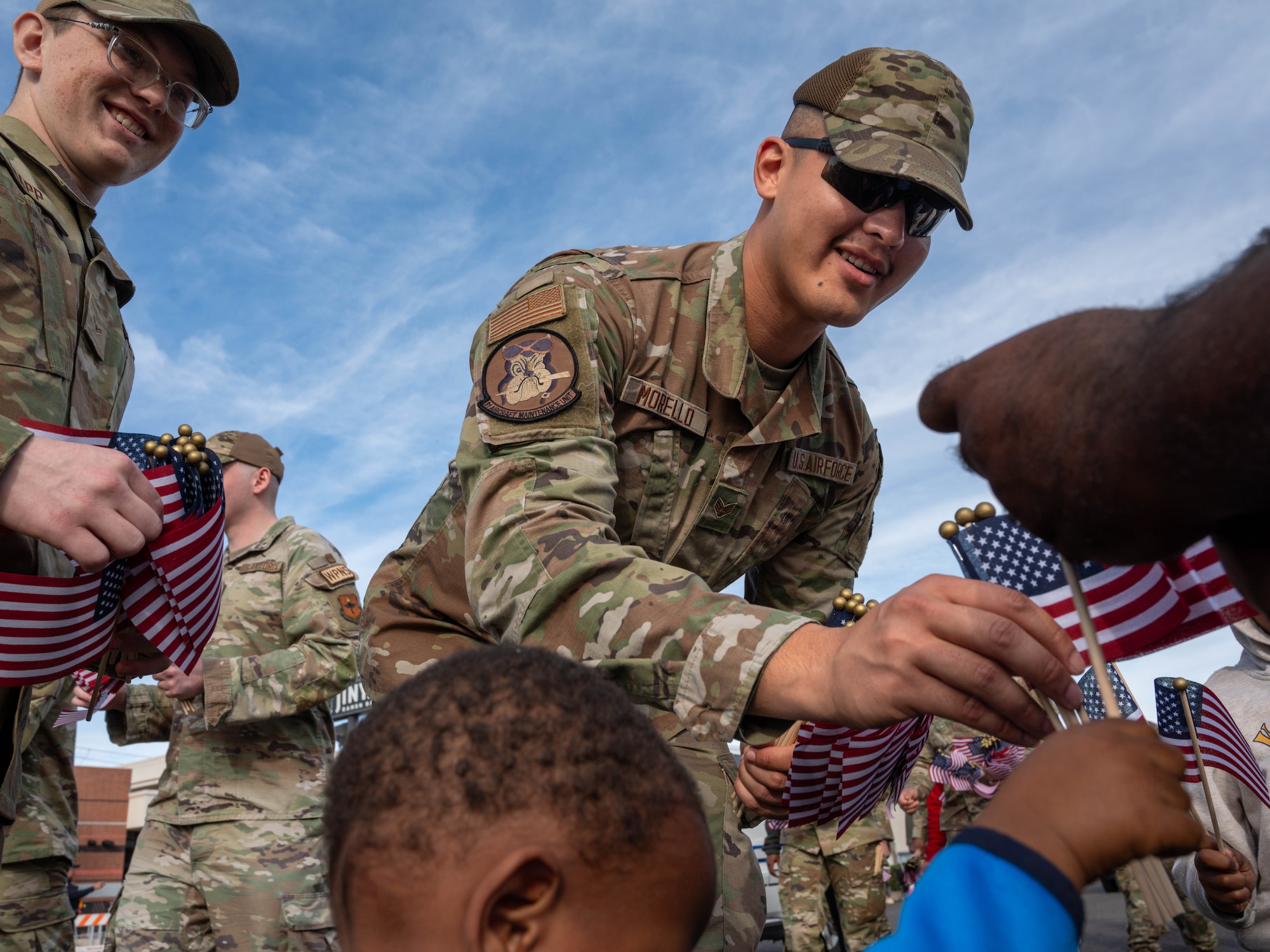 U.S. Air Force Senior Airman Giovanni Morello, 61st Aircraft Maintenance Unit avionics technician, hands out flags to spectators during the Fiesta Bowl Parade, Dec. 16, 2023, in Phoenix, Arizona.