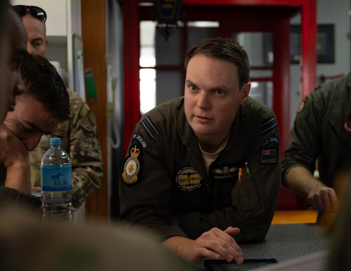 A RNZAF pilot speaks in a brief at a table.