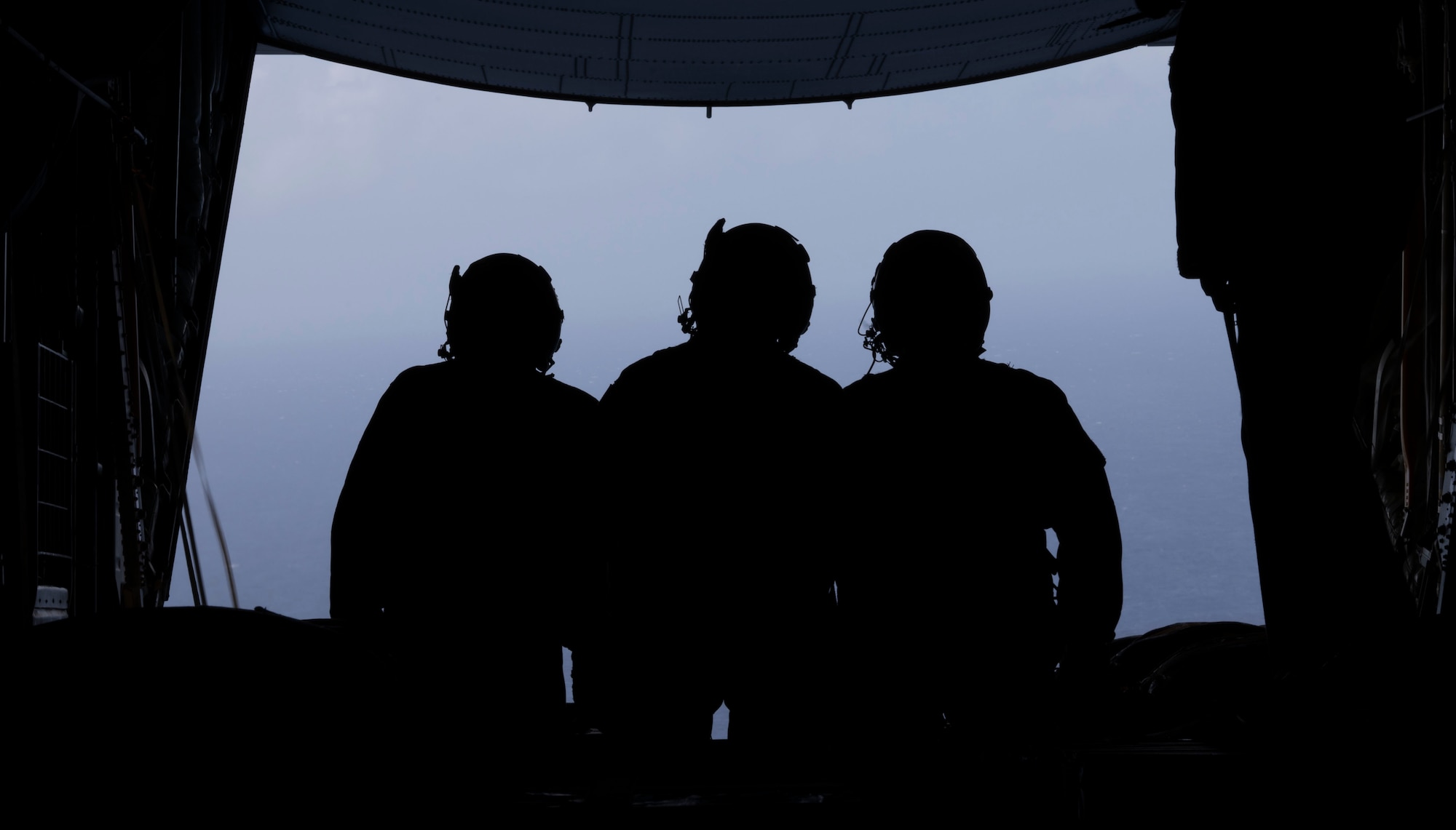 Three silhouettes of airman standing in the back of a C130J Hercules.