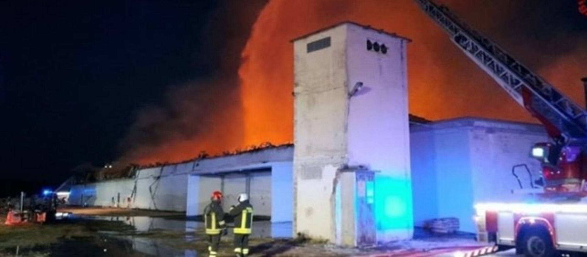 A firetruck sprays water onto a warehouse fire.