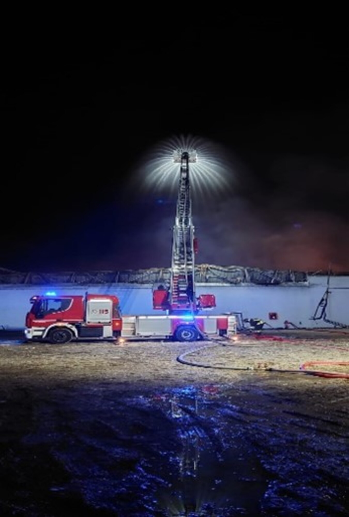A firetruck sprays water onto a warehouse fire.