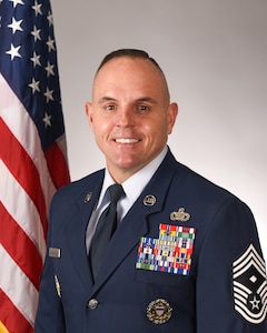 Portrait of man in a military uniform with a flag behind him.