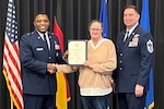 Heike Neumann, center, holds a certificate and shakes hands with Brig. Gen. Otis C. Jones with Command Chief Master Sgt. Louis J. Ludwig on her other side