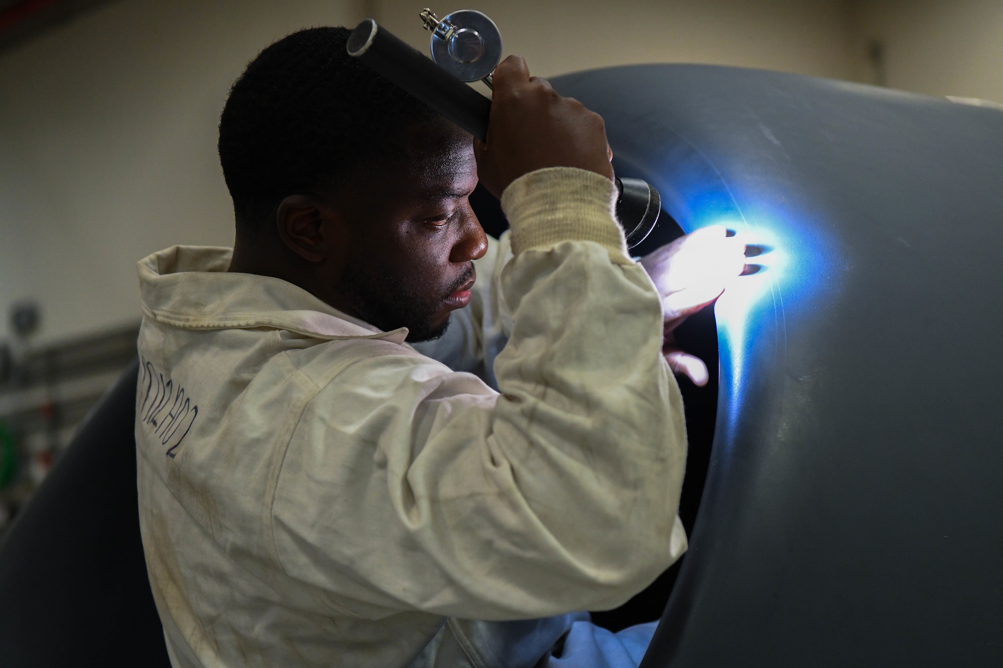 A man shines a flashlight into an aircraft intake.