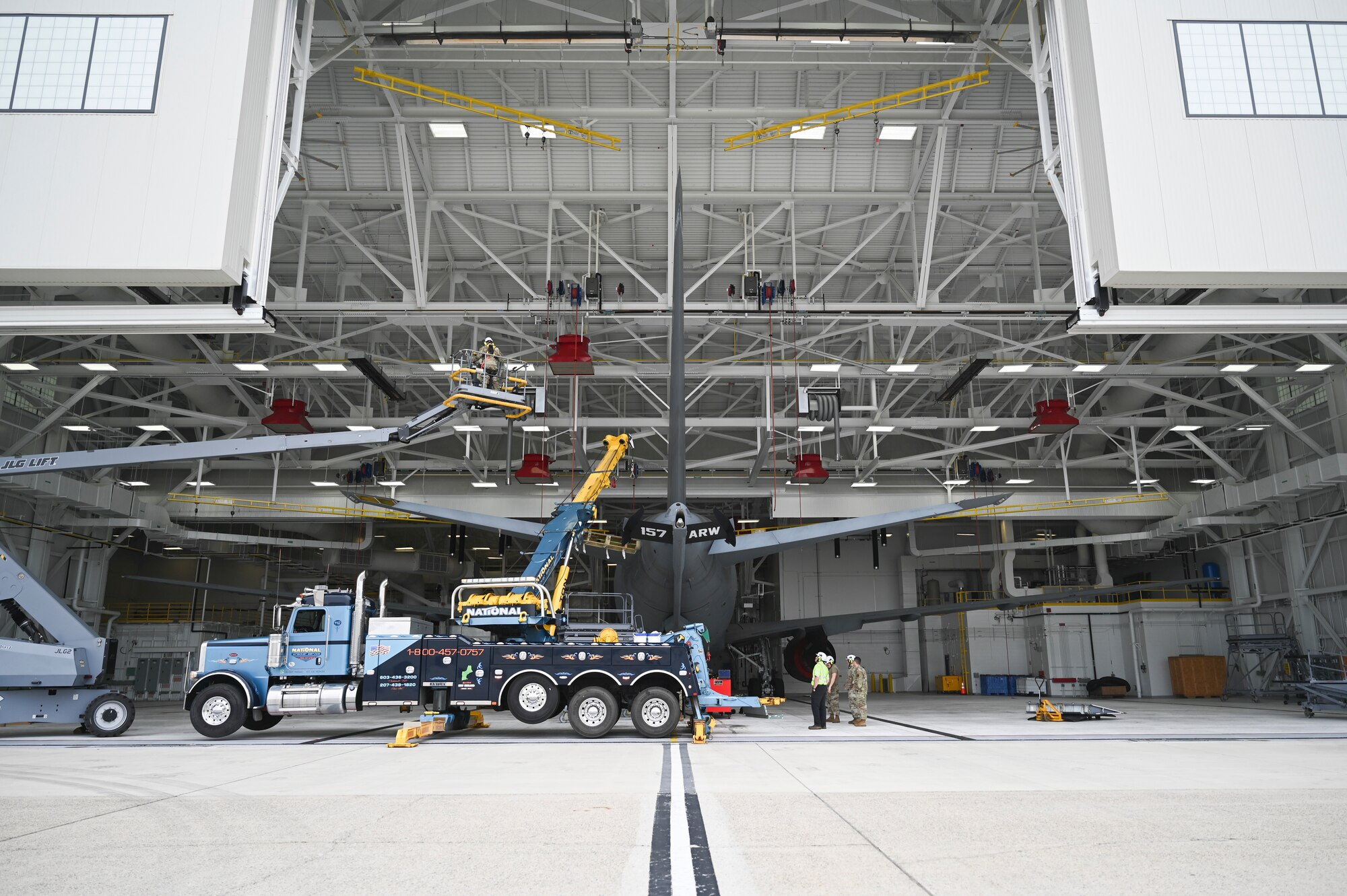 A crane is stationed next to an aircraft inside the hangar door.