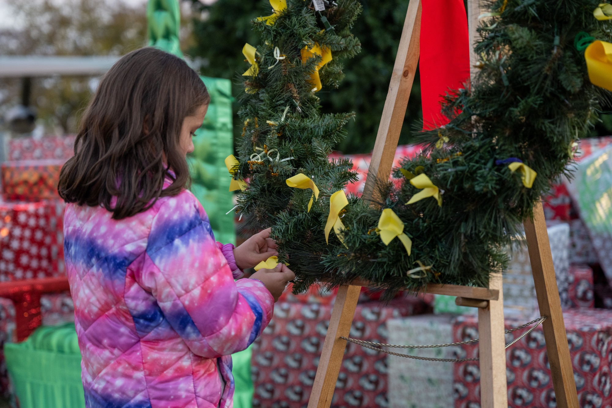 A military child pins a yellow ribbon to a wreath during the Christmas tree lighting ceremony at Hurlburt Field, Florida, Dec. 7, 2023. Children whose family members are currently deployed attached yellow ribbons to a wreath as a tribute to those who were unable to join during the holiday season. (U.S. Air Force photo by the Senior Airman Alysa Calvarese)