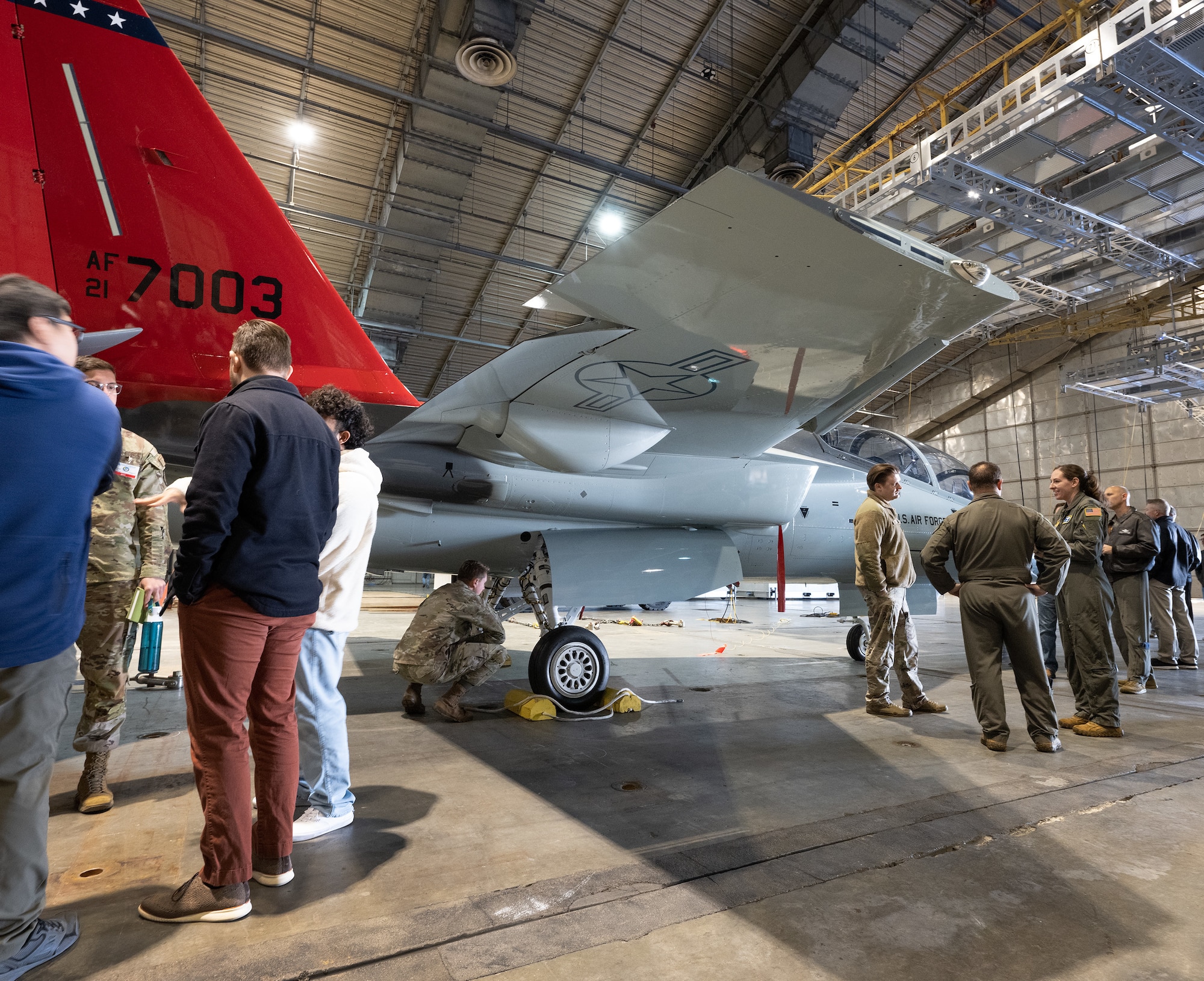 Base personnel gather around the T-7 Red Hawk inside a hangar.