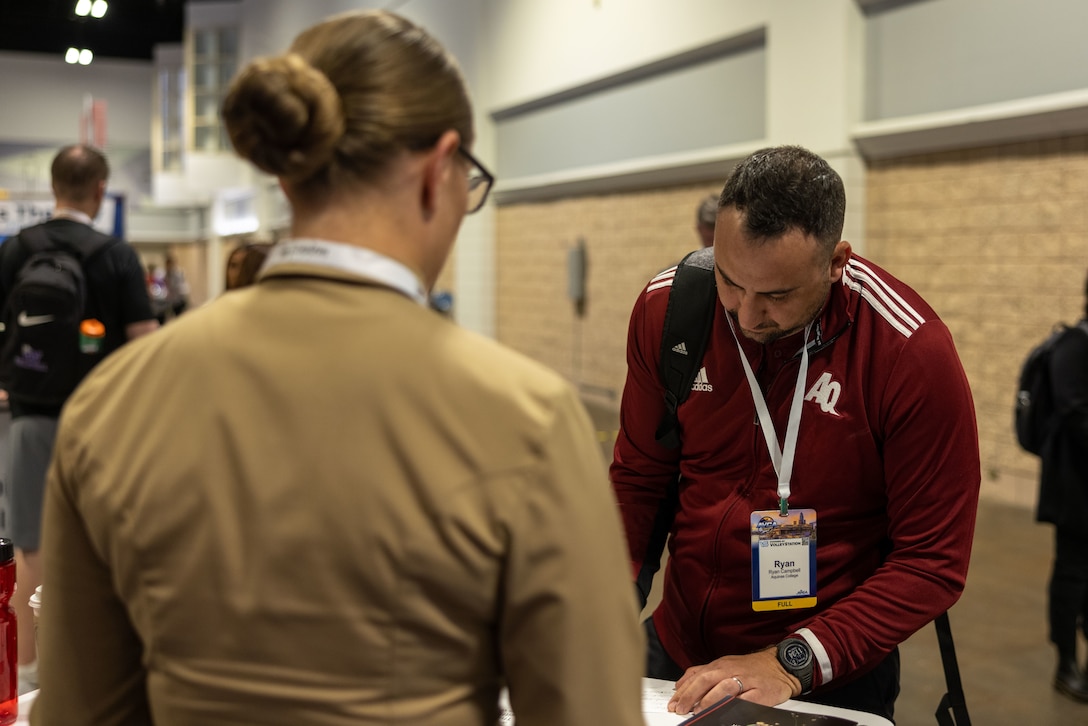 TAMPA, Fla.- U.S. Marine Corps Capt. Caroline Locksmith, a Marine Logistics Officer with Marine Forces Cyber, speaks with Ryan Campbell, the volleyball coach at Aquinas College, during the American Volleyball Coaches Association convention, in Tampa, Fla., on Dec. 14, 2023, about the Marine Corps Recruiting Command’s Coaches Workshop. The Marine Corps National Partnerships ensure the coaches of the next generation of Marines have the resources and skills to accurately present the Marine Corps as an option to their athletes, and support recruiter access to prospective audiences. (U.S. Marine Corps Photo by Lance Cpl. Payton Goodrich)