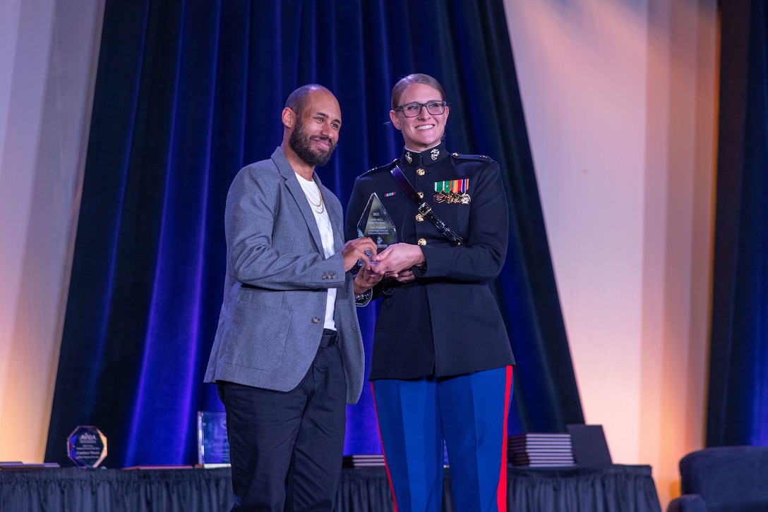 TAMPA, Fla.- U.S. Marine Corps Capt. Caroline Locksmith, a logistics officer with Marine Forces Cyber, presents the battles won award to Chris Wakefield, the Volleyball coach for Godwin High School in Richmond, Va., during the American Volleyball Coaches Association Luncheon in Tampa, Fla., on Dec. 14, 2023. The Marine Corps National Partnerships ensure the coaches of the next generation of Marines have the resources and skills to accurately present the Marine Corps as an option to their athletes, and support recruiter access to prospective audiences. (U.S. Marine Corps Photo by Lance Cpl. Payton Goodrich)