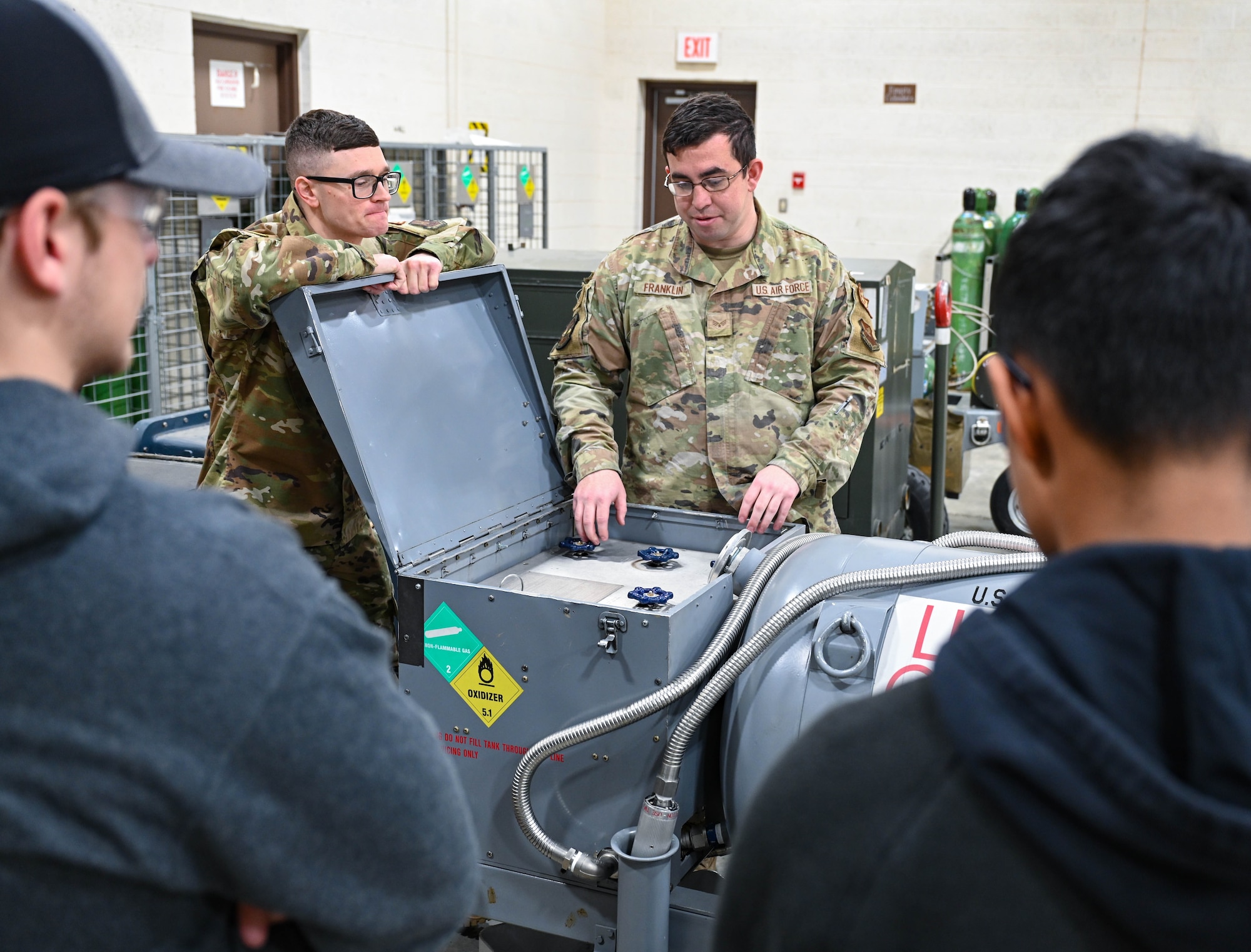 Senior Airmen Morgan Bush, left, and Vincent Franklin, right, 28th Maintenance Squadron B-1B Lancer electrical and environmental systems journeymen, show students from Douglas High School a liquid oxygen cart at Ellsworth Air Force Base, South Dakota, Dec. 12, 2023.