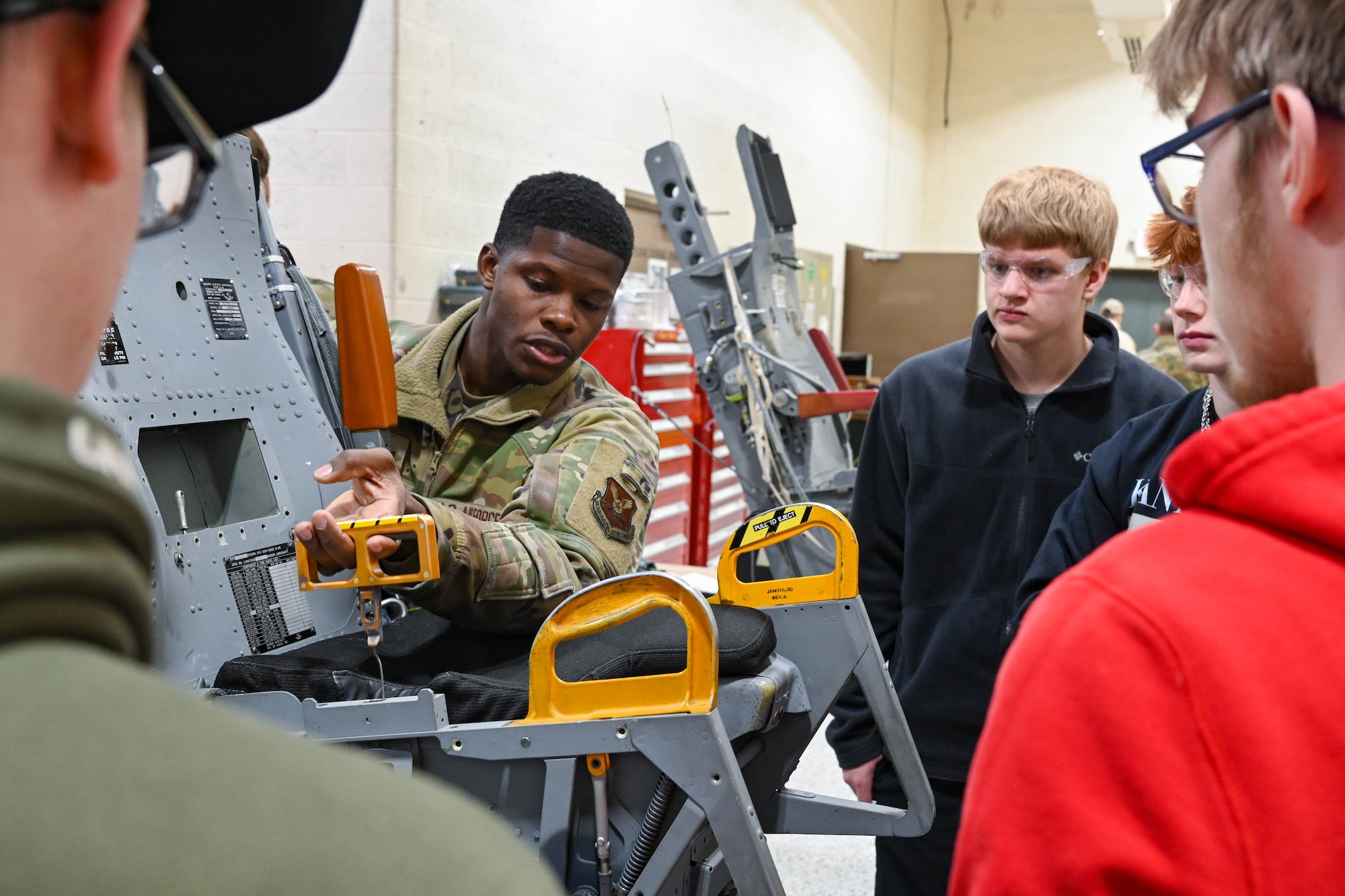 Senior Airman Jahmari Cromartie, 28th Maintenance Squadron egress systems journeyman, demonstrates how to activate the ejection feature on a B-1B Lancer seat for students from Douglas High School at Ellsworth Air Force Base, South Dakota, Dec. 12, 2023.
