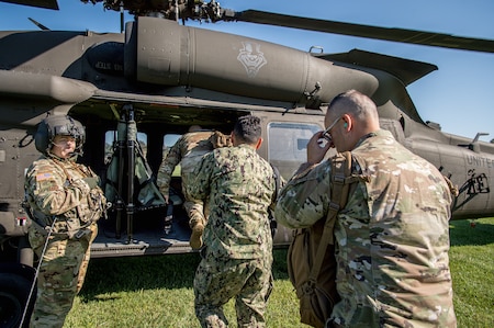 Several Army soldiers in fatigues are loading into a UH-60 Blackhawk helicopter that is parked on a green lawn.