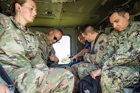 Several Army soldiers in fatigues are adjusting their seatbelts while sitting inside a UH-60 Blackhawk helicopter