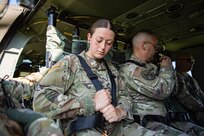 Several Army soldiers in fatigues are adjusting their seatbelts while sitting inside a UH-60 Blackhawk helicopter