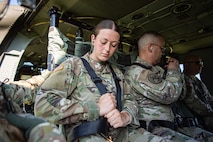 Several Army soldiers in fatigues are adjusting their seatbelts while sitting inside a UH-60 Blackhawk helicopter