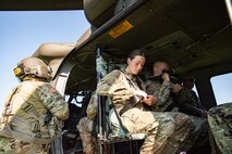 Several Army soldiers in fatigues are adjusting their seatbelts while sitting inside a UH-60 Blackhawk helicopter