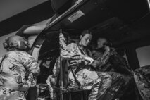 Several Army soldiers in fatigues are adjusting their seatbelts while sitting inside a UH-60 Blackhawk helicopter