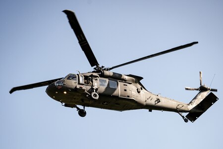 a UH-60 Blackhawk helicopter is hovering near the National Defense University with light blue sky in the background