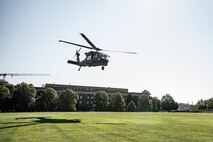 a UH-60 Blackhawk helicopter is hovering, about to land, on a green lawn near the National Defense University