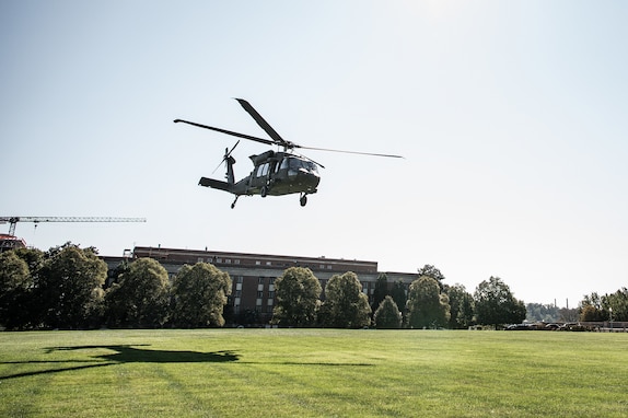 a UH-60 Blackhawk helicopter is hovering, about to land, on a green lawn near the National Defense University