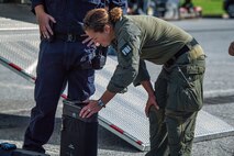 A member of the FBI is kneeling over a device and has her hand on it, while someone wearing an all-blue utility outfit is nearby and watching.