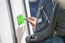 A member of the FBI is using a black sharpie to write something on a bright green sticker that is affixed to plastic container.