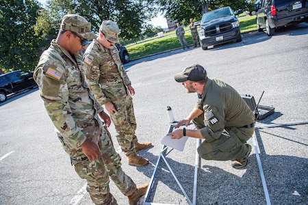 Two Army service members are standing near a member of the FBI as they assemble a large metal frame in a parking lot.