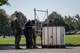 Four Service members from 55th Explosive Ordinance Disposal (EOD) Company and EOD agents from the FBI’s Washington Field Office are standing near a metal frame, which is near a large square-shaped plastic container.
