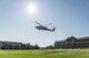 UH-60 helicopter is hovering over a green lawn in front of the National War college building, which is a large, red brick building with a dome in the middle