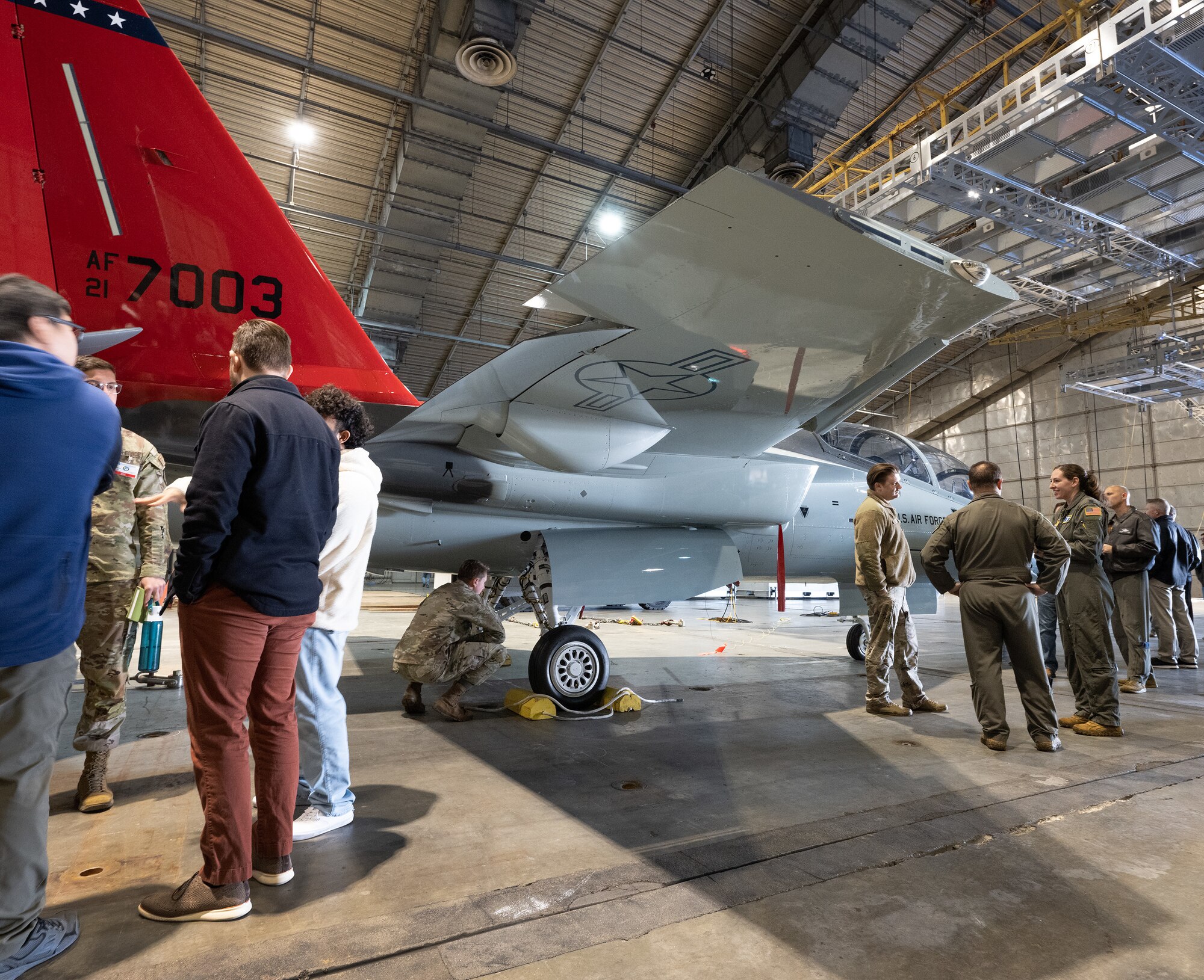 Base personnel gather around the T-7 Red Hawk inside a hangar.