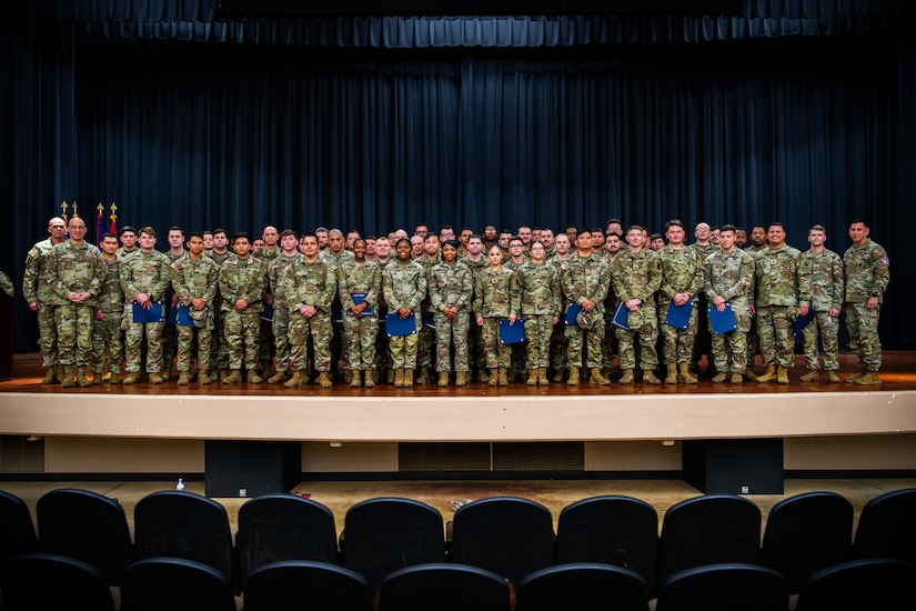 Large group of U.S. Army soldiers stand on stage after a graduation and promotion ceremony