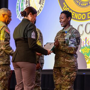 A female in a U.S. Army uniform hands another female soldier an award