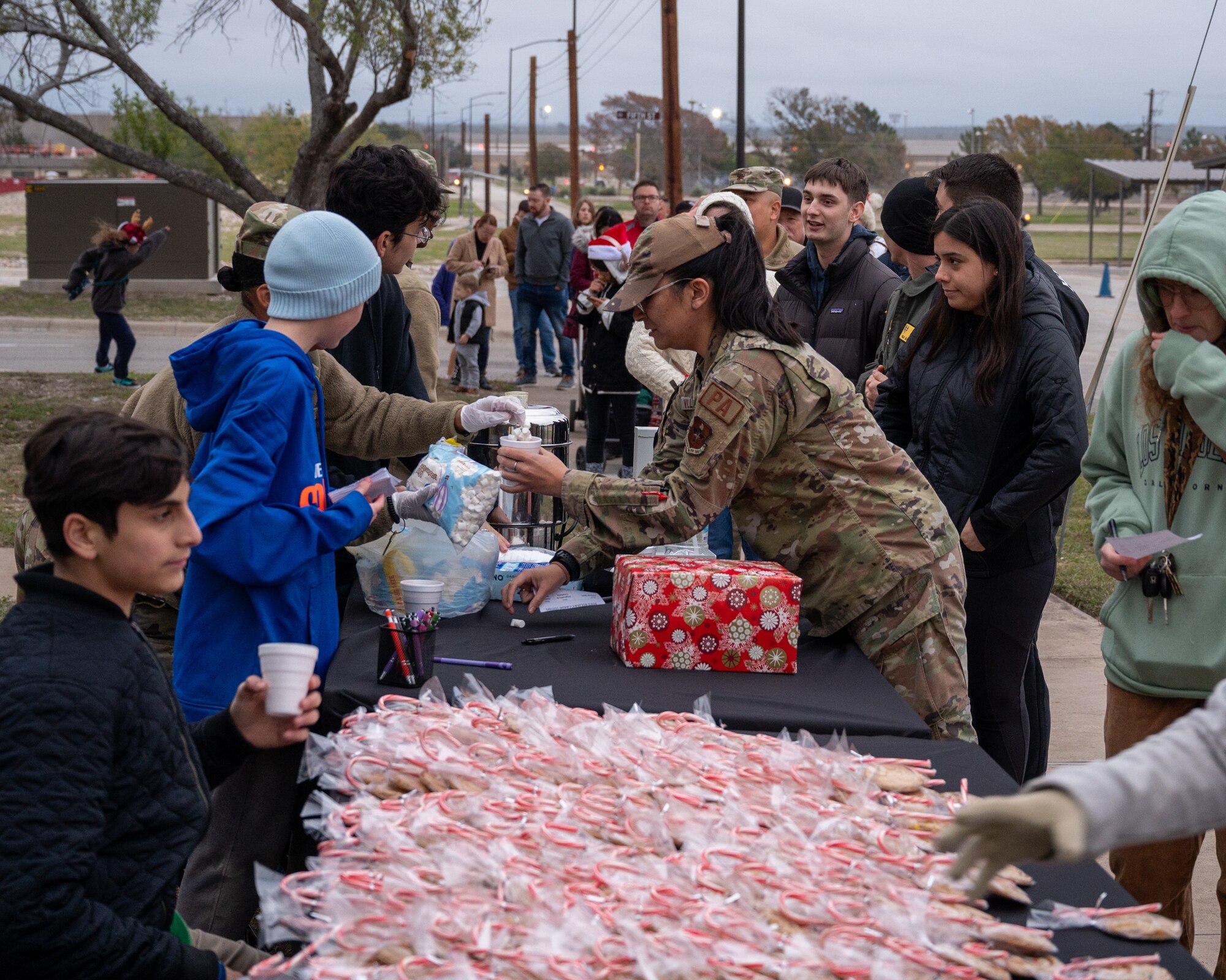 Children and Airmen grab a cookie, candy cane and hot coco from the table outside of the chapel for the tree lighting ceremony at Laughlin Air Force Base, Texas, Nov. 29, 2023. The ceremony brings together Airmen and their families for a festive occasion to celebrate the holiday season. (U.S. Air Force photo by Staff Sgt. Nicholas Larsen)