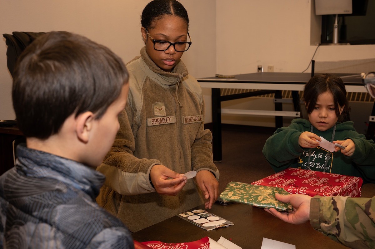U.S. Air Force Airman 1st Class Alonni Spradley, Installation Entry Controller from the 354th Security Forces Squadron, helps children wrap presents as part of "Shop with a Cop" on Eielson Air Force Base, Alaska, Dec. 17 2023. This event aims to create positive community relations between law enforcement and the younger generation. (U.S. Air Force Photo by Airman Spencer Hanson)