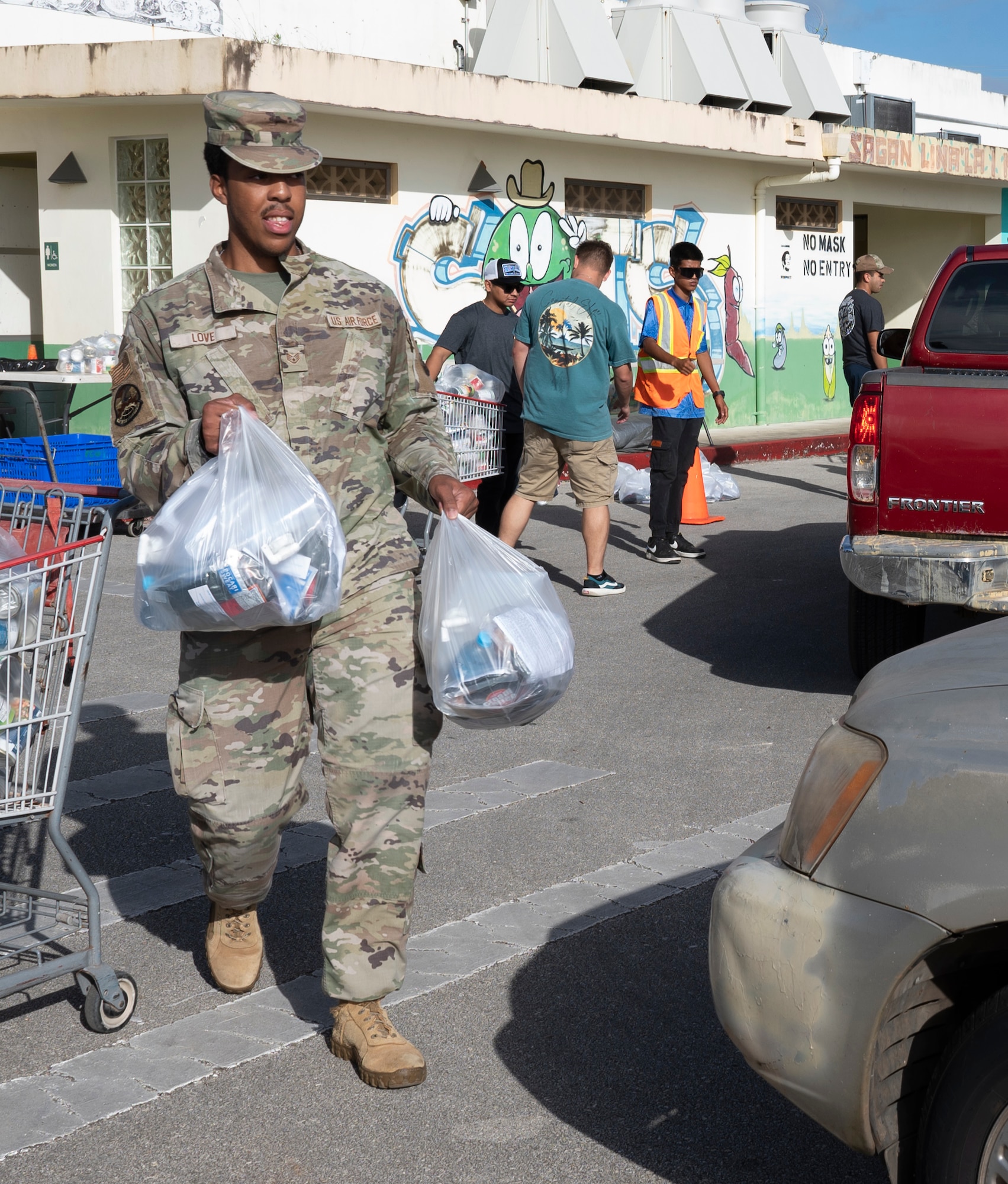 U.S. Air Force Staff Sgt. Christian Love, 734th Air Mobility Squadron commander support staff noncommissioned officer in charge, carries food to a local family during a volunteer event in Dededo, Guam, December 15, 2023. The 734 AMS volunteered to help Dededo as part of the Sister Village Sister Squadron program. They collected food, toiletry, and lifesaving equipment donations and helped hand them out to local families. (U.S. Air Force photo by Airman 1st Class Spencer Perkins)