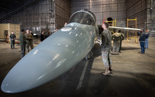 A T-7 Red Hawk rests inside a hangar, while base personnel walk around to view it.