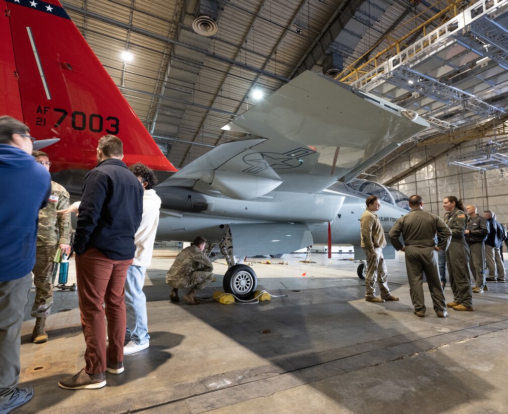 Base personnel gather around the T-7 Red Hawk inside a hangar.