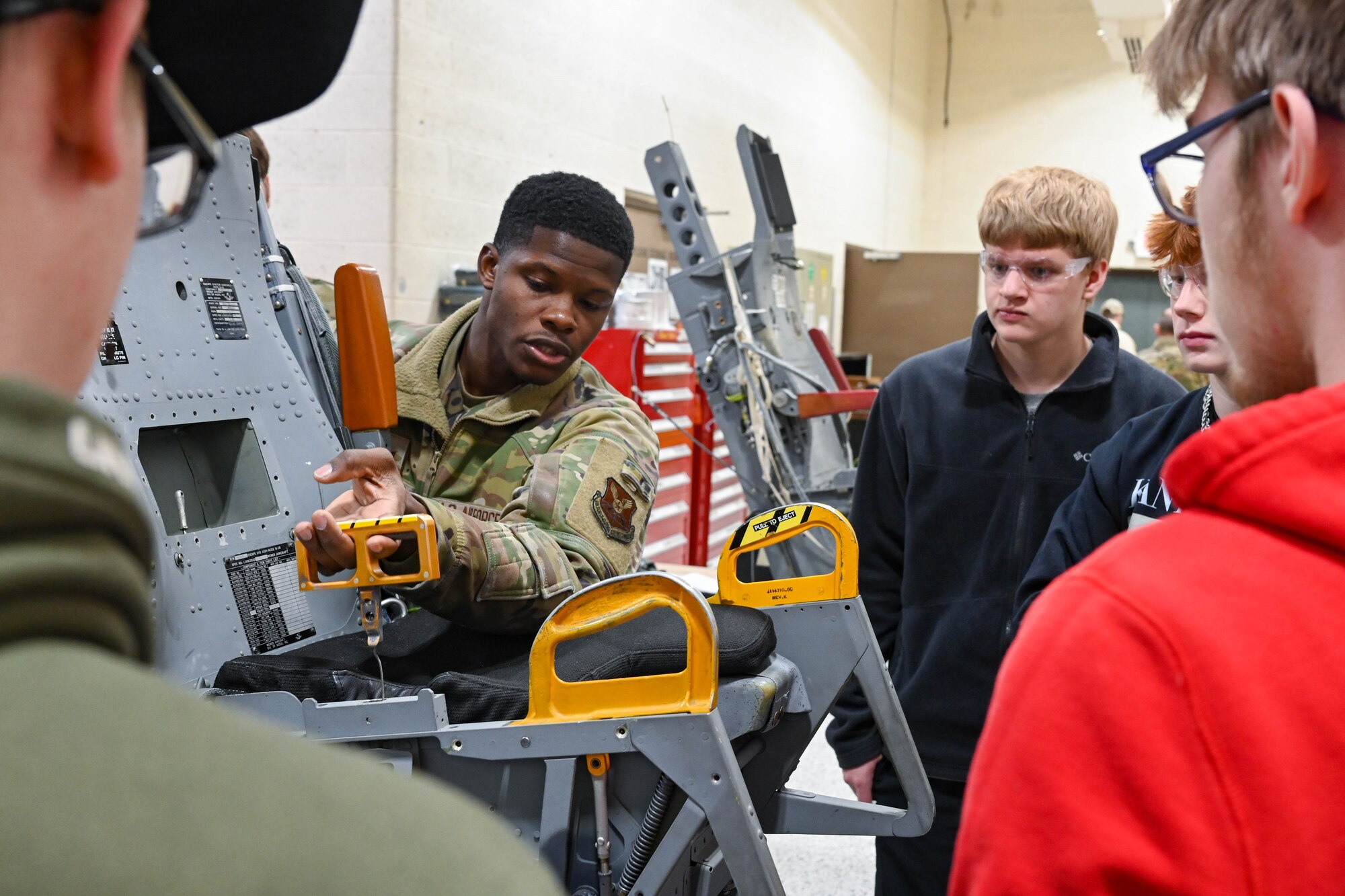Senior Airman Jahmari Cromartie, 28th Maintenance Squadron egress systems journeyman, demonstrates how to activate the ejection feature on a B-1B Lancer seat for students from Douglas High School at Ellsworth Air Force Base, South Dakota, Dec. 12, 2023.