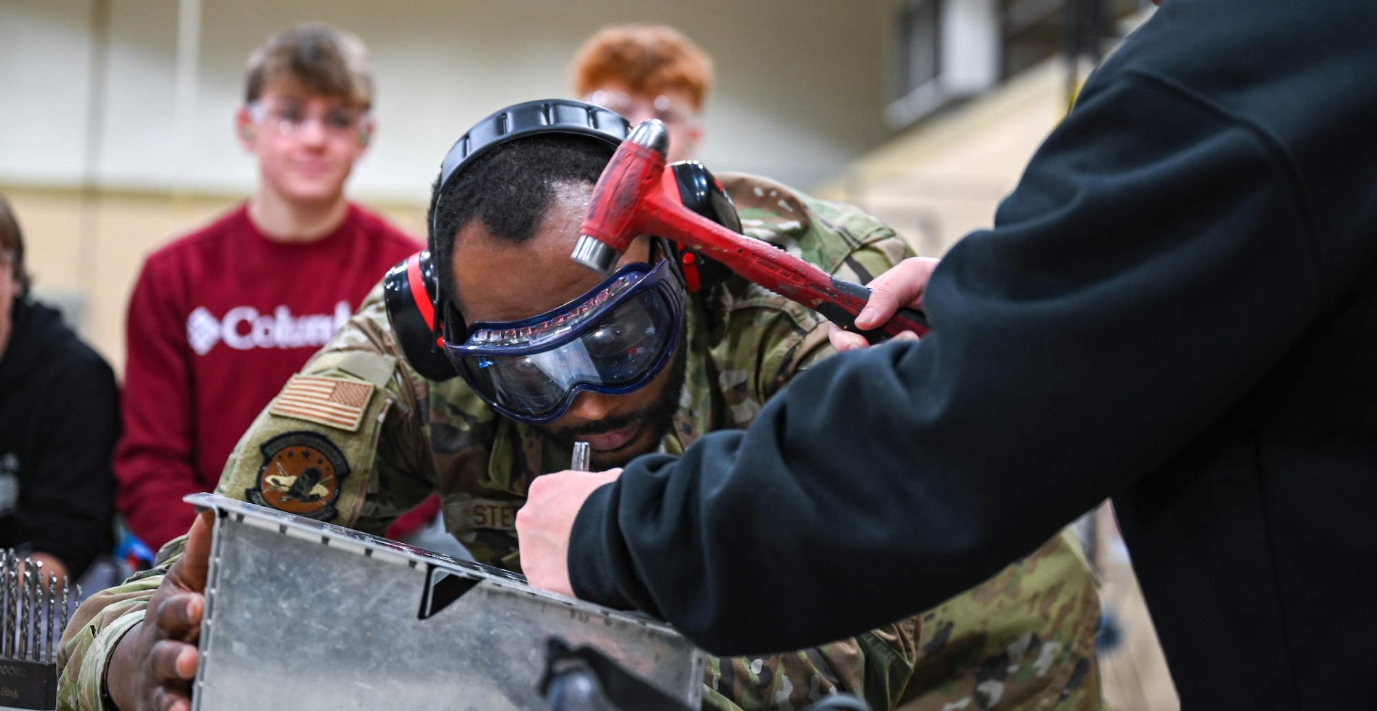 Senior Airman Stepheon Stewart, 28th Maintenance Squadron aircraft structural maintenance journeyman, supervises a student from Douglas High School as he hammers a punch to remove fasteners from a sheet metal box at Ellsworth Air Force Base, South Dakota, Dec. 12, 2023.