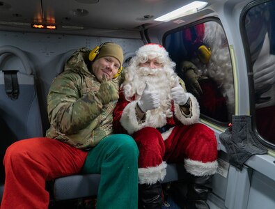 Santa is sitting next to a service member in an aircraft