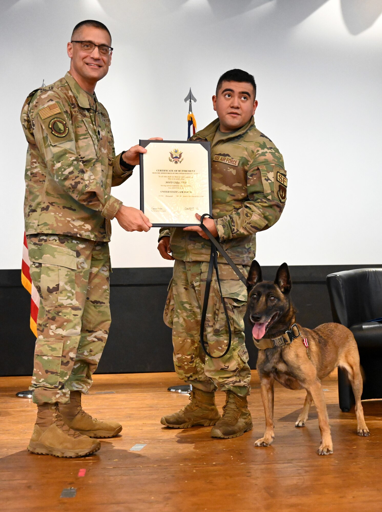 U.S. Air Force Lt. Col. Ben Washburn, left, 48th Security Forces Squadron commander, presents a Certificate of Appreciation signed by the Secretary of the Air Force, to Military Working Dog Ukkie, 48th SFS, during her retirement ceremony at Royal Air Force Lakenheath, England, Dec. 13, 2023. Ukkie, who also received a Meritorius Service Medal, began her active-duty career in 2017, serving at RAF Mildenhall with the 100th Security Forces Squadron, before being transferred to the RAF Lakenheath kennels in 2020. She has been adopted by her first handler at RAF Mildenhall, and will live out her days with her family in Virginia. (U.S. Air Force photo by Karen Abeyasekere)