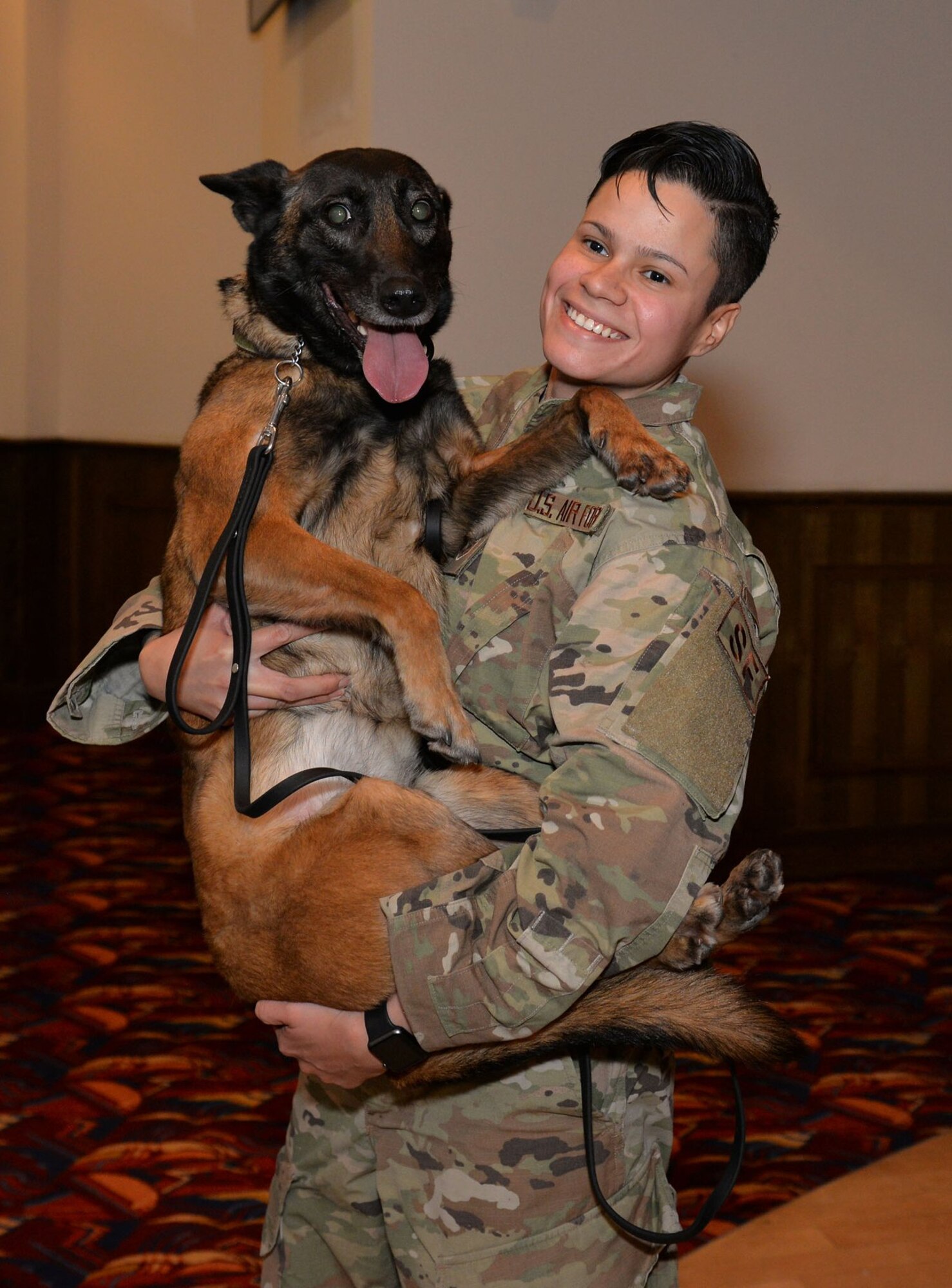 U.S. Air Force Military Working Dog Ukkie shows a look of utter joy as she is held by former 100th Security Forces Squadron handler, then-Staff Sgt Kristina Santos, at the retirement ceremony of MWD Vvonya at Royal Air Force Mildenhall, England, Jan. 18, 2019. Ukkie was part of a dog swap with RAF Lakenheath in 2020 and has been assigned to the 48th Security Forces Squadron kennels since then, retired from active-duty service at a ceremony Dec. 13, 2023. She has been adopted by Santos, now a civilian dog trainer, and is ready to put her paws up at her forever-home in Virginia. (U.S. Air Force photo by Karen Abeyasekere)