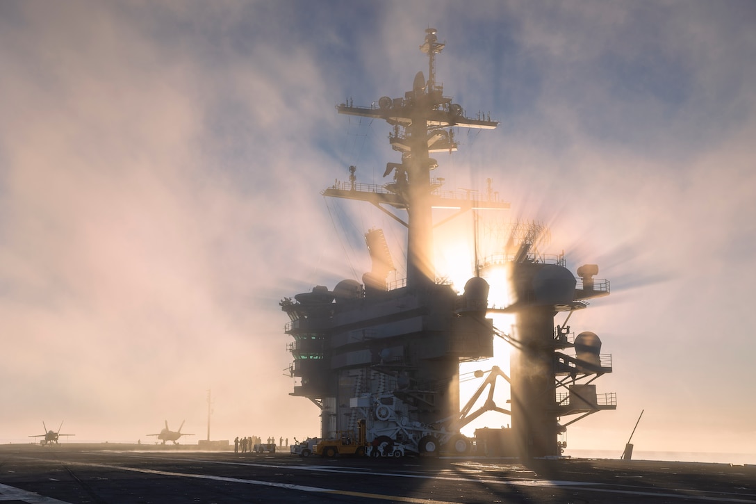 Sunlight beams through the clouds and hits an aircraft carrier .