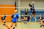 Air Force athlete returns a volleyball across the net with the opposing squad poised to block its return.