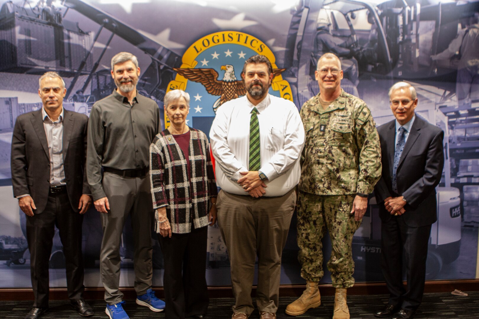 People standing in front of a Defense Logistics Agency logo mural.