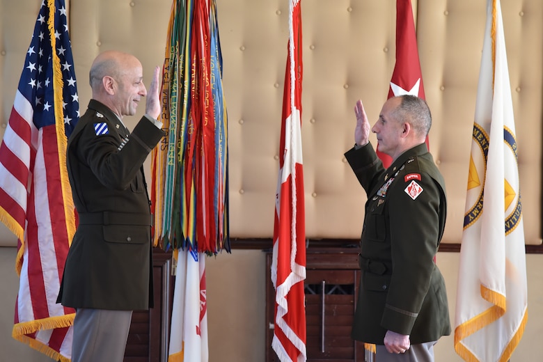 Two men in Army uniforms stand across from each other, each with their right hand raised.